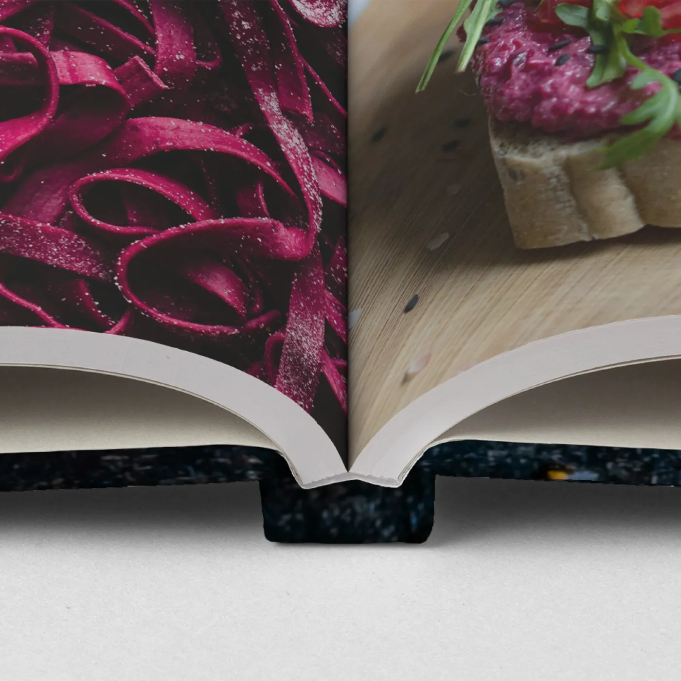 Book binding detail showing beet colored pasta on one page and other food on the opposite page.