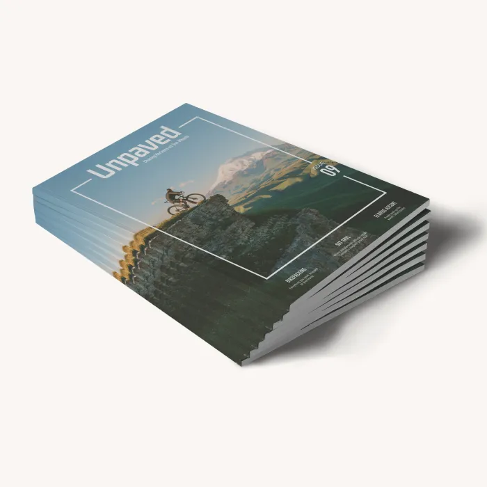 Ein Stapel Zeitschriften mit dem Titel „Unpaved“, auf deren Cover eine schöne Landschaft und ein Radfahrer zu sehen sind.