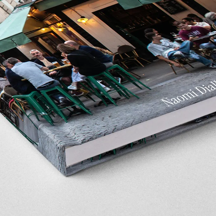 Hardcover-Fotobuch mit bedrucktem Umschlag (ImageWrap), geöffnet mit Panoramaaufnahme des Eiffelturms über drei Viertel der Doppelseite, rechts Text.