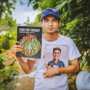 Eine junge Person mit Baseballmütze hält im Freien bei natürlicher Beleuchtung das Kochbuch „Food for Thought“ in der Hand.