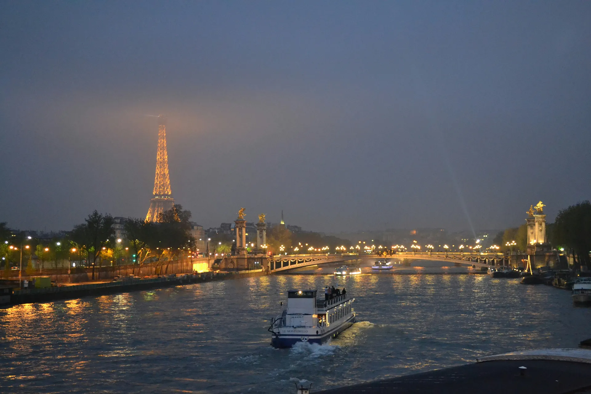 A scenic view of the Seine River at night with the Eiffel Tower illuminated in the background.