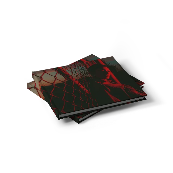 A stack of two landscape, hardcover photo books. The cover shows a dark photo with a red filter, of a person next to a fence