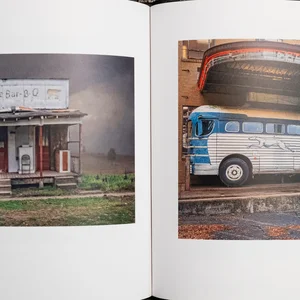 Clay Fisher's square photo book, SlowExposures 2023, open on photos of an old roadside BBQ shack and an old greyhound coach