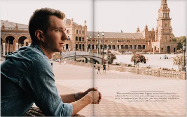 Full-spread photo of a man sitting at a table in a sunlit European plaza.