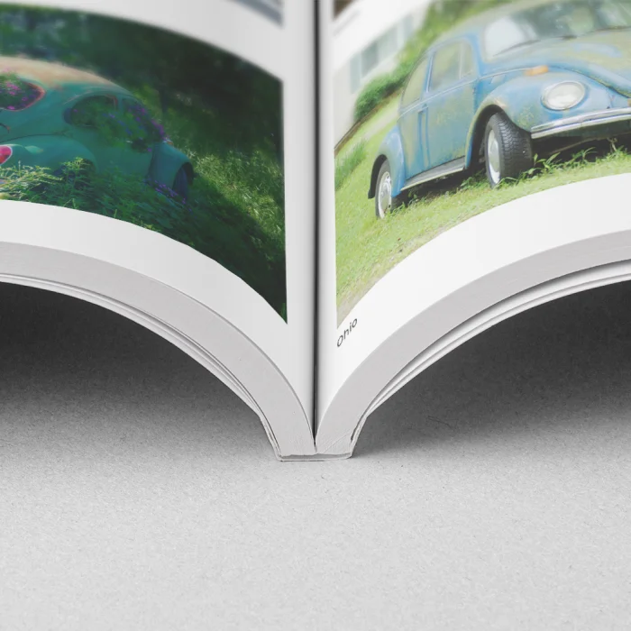 Nahaufnahme der Bindung eines aufgeschlagenen Softcover-Buches mit Fotos eines klassischen blauen Autos auf einer Doppelseite