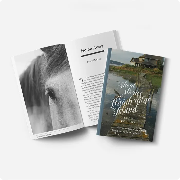 Two copies of 'Short Stories of Bainbridge Island' by Oyster Seed Salon, one open showing interior text and a black-and-white photo, the other closed showing the cover image of a waterfront house