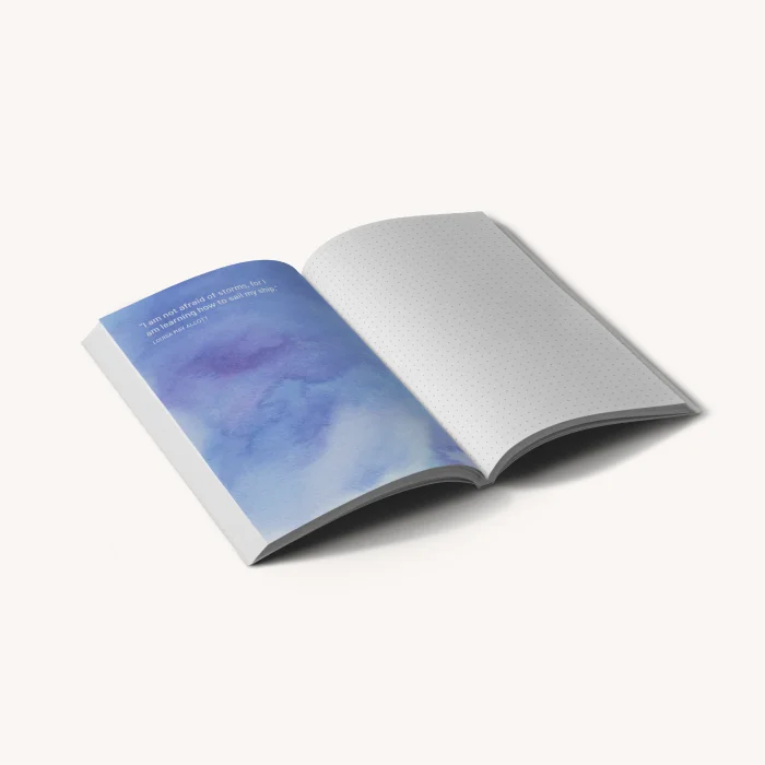 Ein aufgeschlagenes Softcover-Notizbuch, in dem links eine mit blauer Wasserfarbe gestaltete Seite und rechts eine Seite mit Punktraster zu sehen ist.