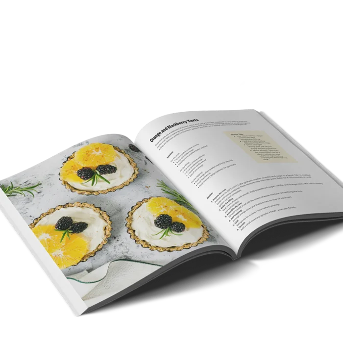 A portrait softcover cookbook open on a recipe for Orange and Blueberry tarts including a photo of three pre-made tarts