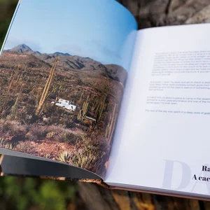 Ein aufgeschlagenes Reisebuch, in dem eine Wüstenlandschaft mit Kakteen und beschreibender Text zu sehen sind.