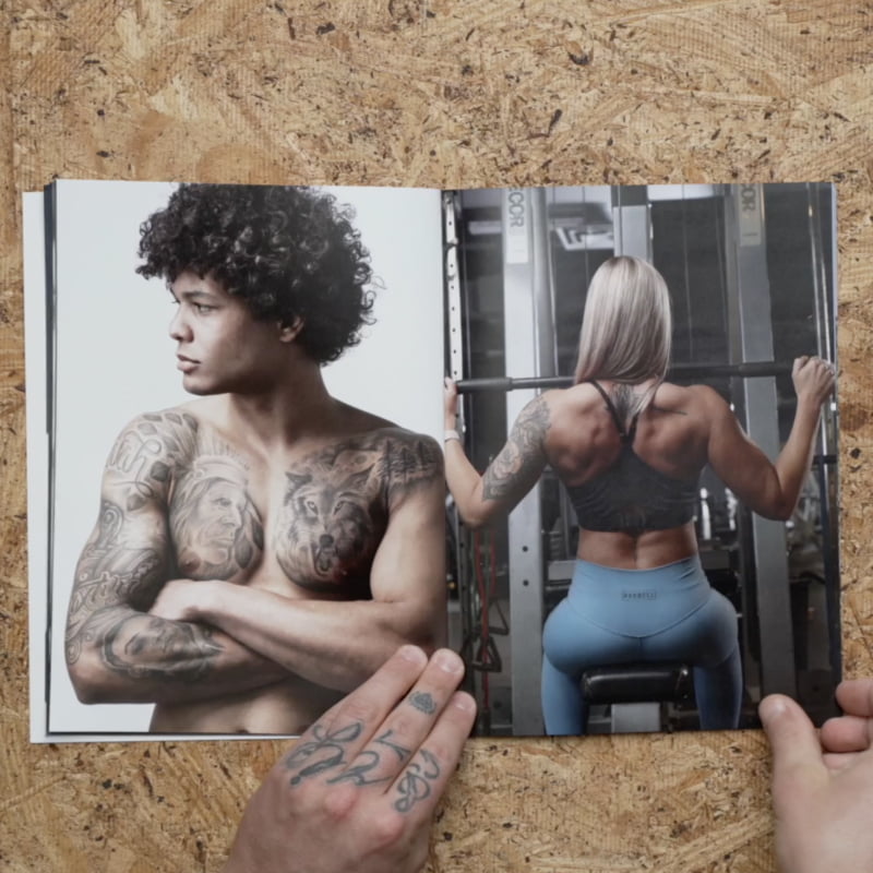 Revista diseñada profesionalmente. Está abierta y muestra la foto de dos personas; una está entrenando en el gimnasio y la otra posa con sus tatuajes.