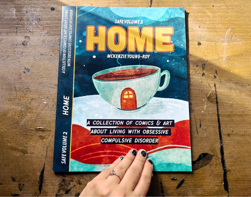 Custom designed magazine titled Safe Volume 2, Home, by McKenzie Young-Roy, A collection of comics and art about living with obsessive compulsive disorder, featuring an illustrated coffee cup with a door drawn on the side.