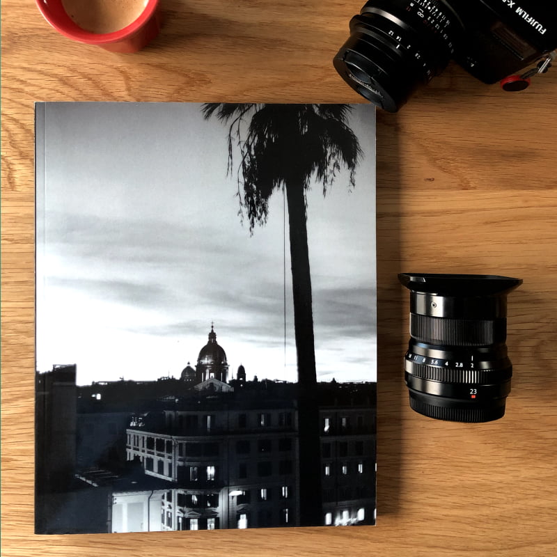 Photo book with a black and white image on the cover next to a lens and a camera